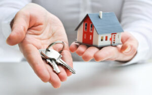 A person holding keys next to a small model of a house.