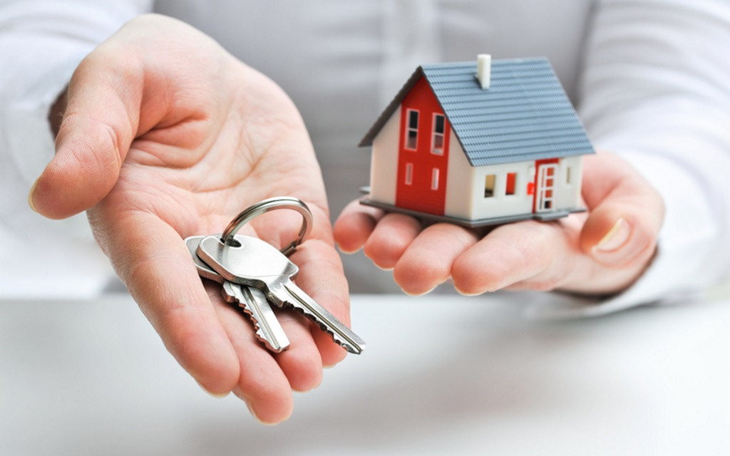 A person holding keys next to a small model of a house.