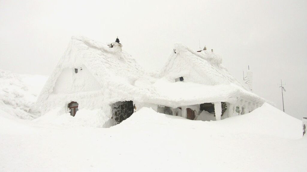 Snow-covered house on a hillside, surrounded by a winter landscape.