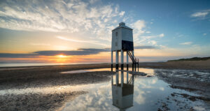 Lighthouse on the beach at sunset, casting a warm glow.