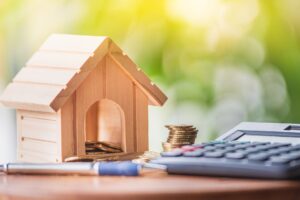 House model with coins and calculator on a wooden table.