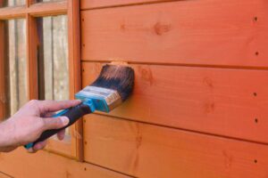 Person painting a wooden house with a brush.