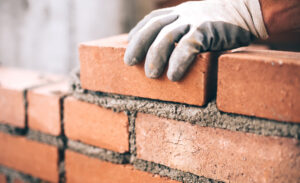 A person in gloves carefully places bricks on a wall.