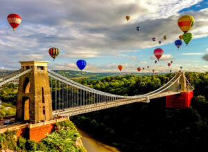 Colourful balloons soaring above a bridge against a clear sky.