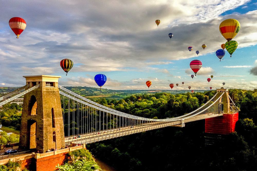 Balloons soaring above a suspension bridge against a clear sky.