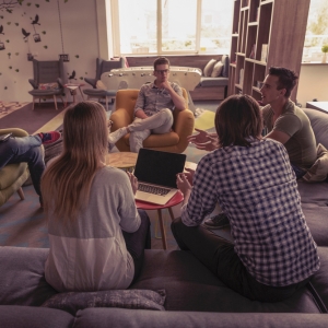 A group of students gathered around a couch in a cosy living room