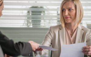 A woman hands a stack of papers to another woman in a professional setting