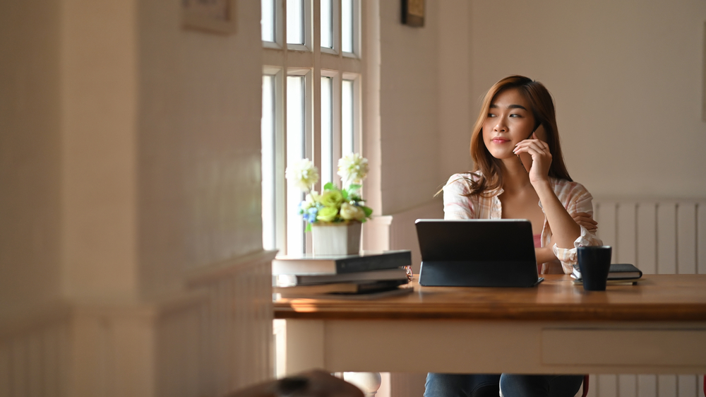 A student seated at a table, using a laptop and phone.