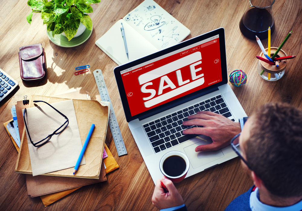 Man using laptop at desk with a sale sign visible.