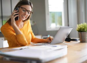 a woman sitting at a table with a laptop and a cell