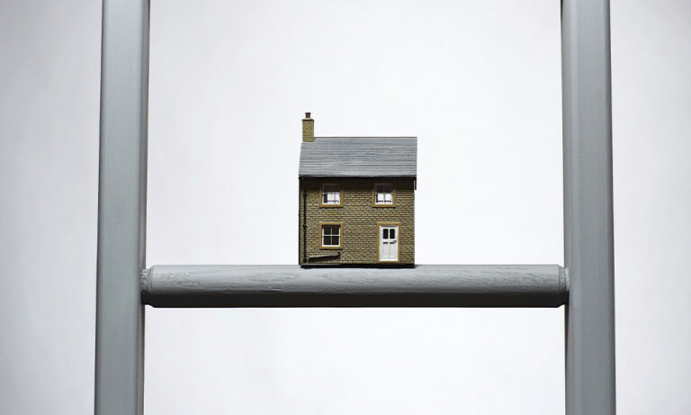 A miniature house perched on a ladder, creating a whimsical and imaginative scene.