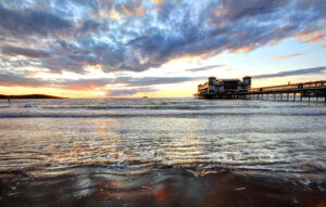 A serene pier at sunset, with gentle waves and soft clouds.