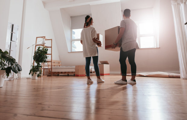 Two individuals transporting boxes in a vacant room.