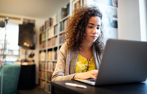A woman with curly hair working on a laptop at a table.